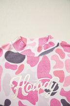 White cursive Howdy text graphic in distressed font overlaid on pink grey camo print