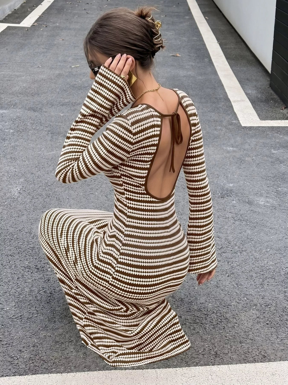 Rückansicht der hockenden Modellin zeigt das offene Rückenausschnitt-Design mit dünnem Bindeverschluss am braunen Kleid