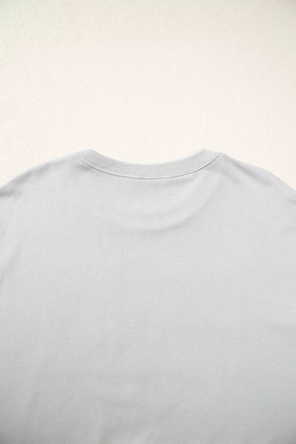 Top-down close-up of back neckline showing standard ribbed crew neck collar and smooth, solid light grey fabric texture