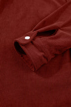 Close-up of deep rust-red sleeve cuff with white button and vertical fabric ridges
