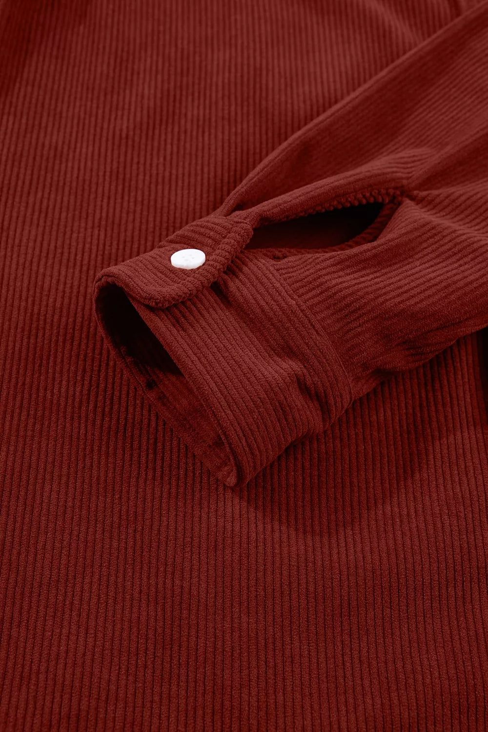 Close-up of deep rust-red sleeve cuff with white button and vertical fabric ridges