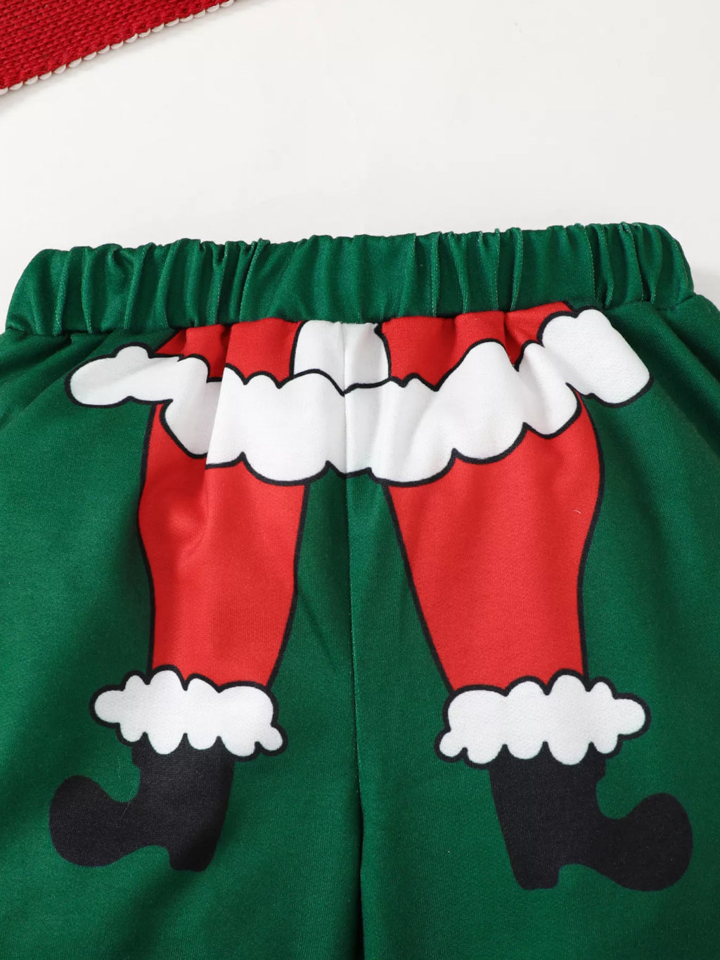 Close up of green sweatpants elastic waistband and humorous graphic of Santa's red trousers with white fur trim and black