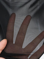 Macro detail of hand behind black mesh fabric revealing skin tone through tight grid-like weave