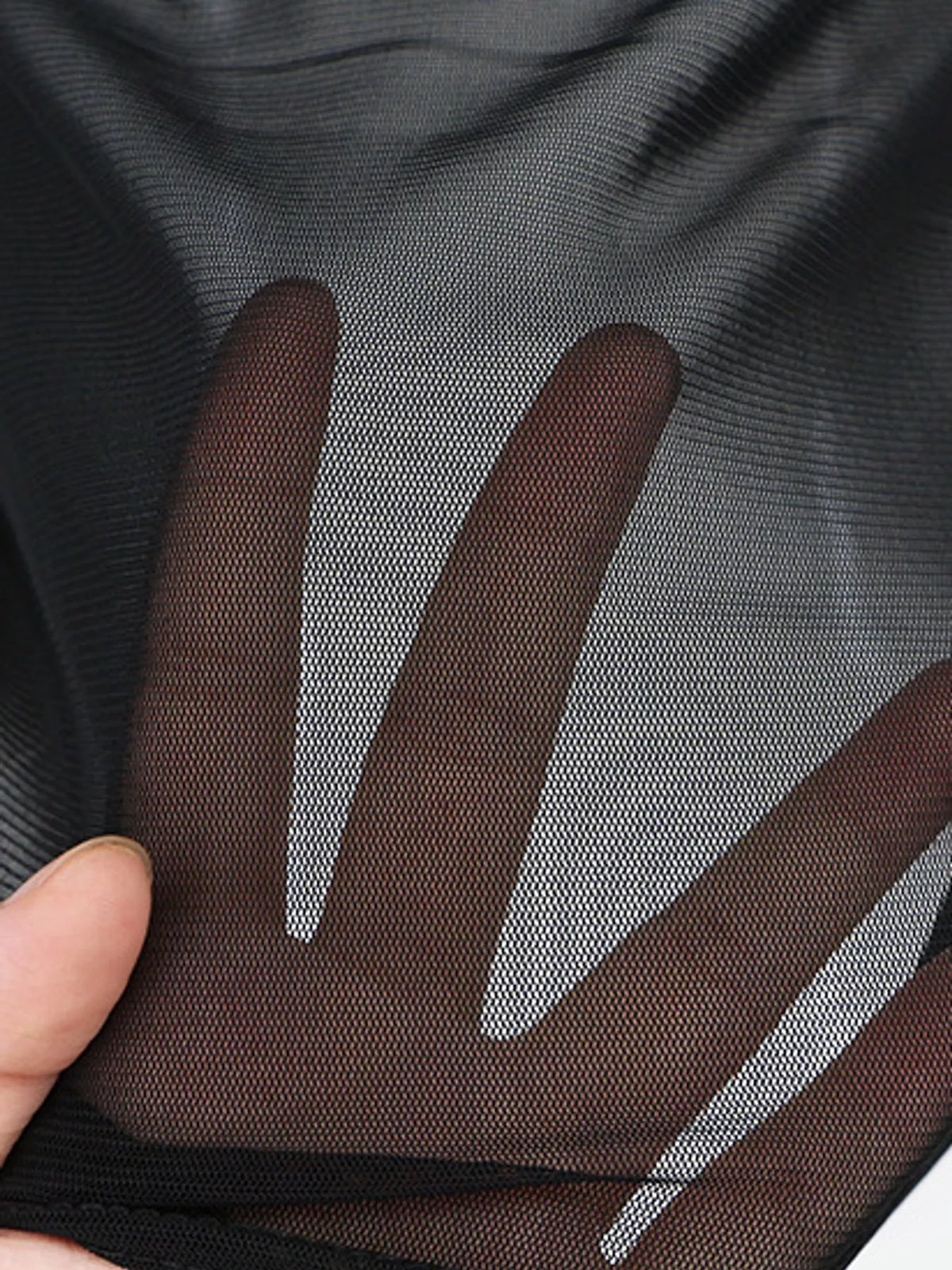 Macro detail of hand behind black mesh fabric revealing skin tone through tight grid-like weave