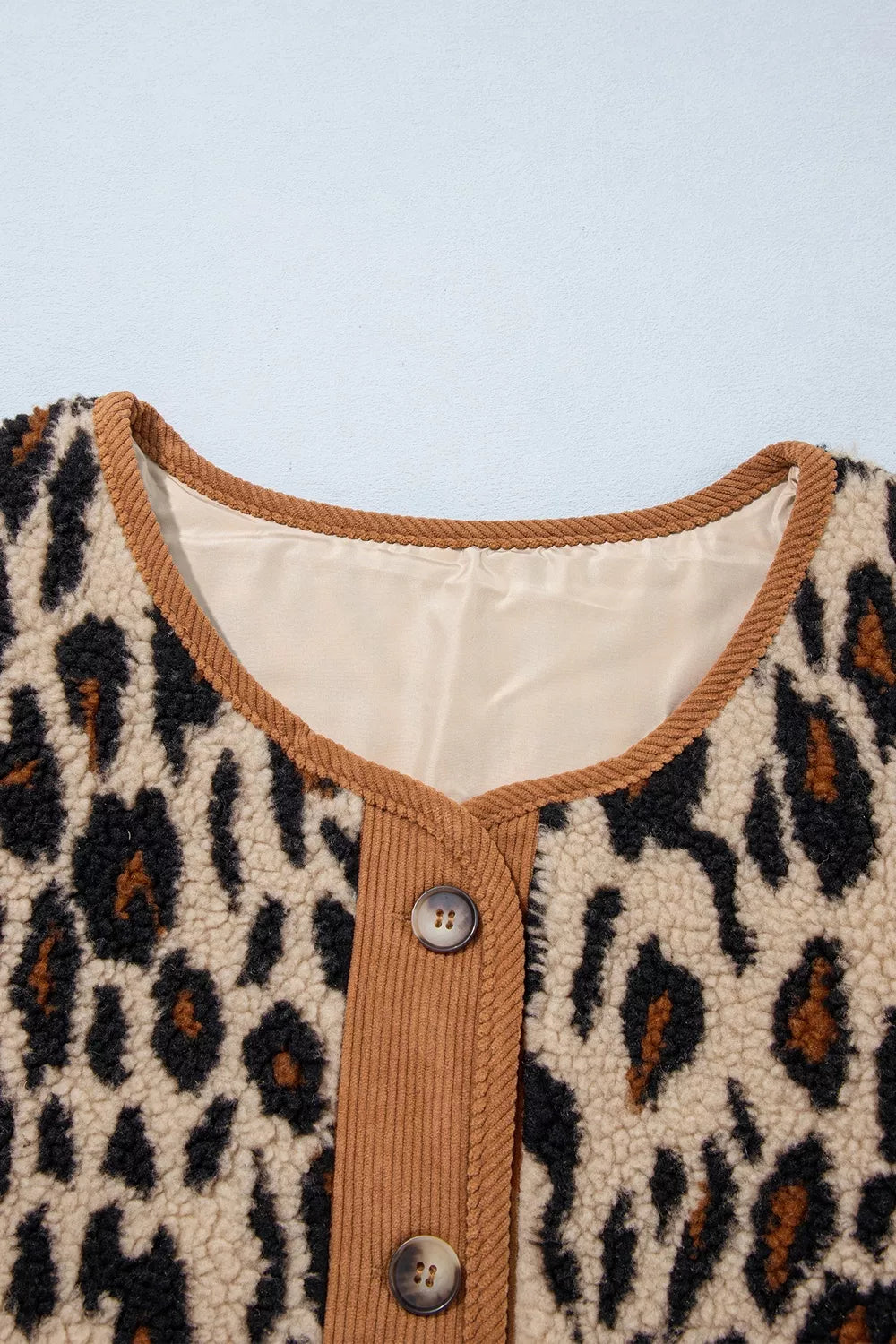 Detail of beige satin lining inside ribbed brown corduroy collar with marbled brown buttons on placket