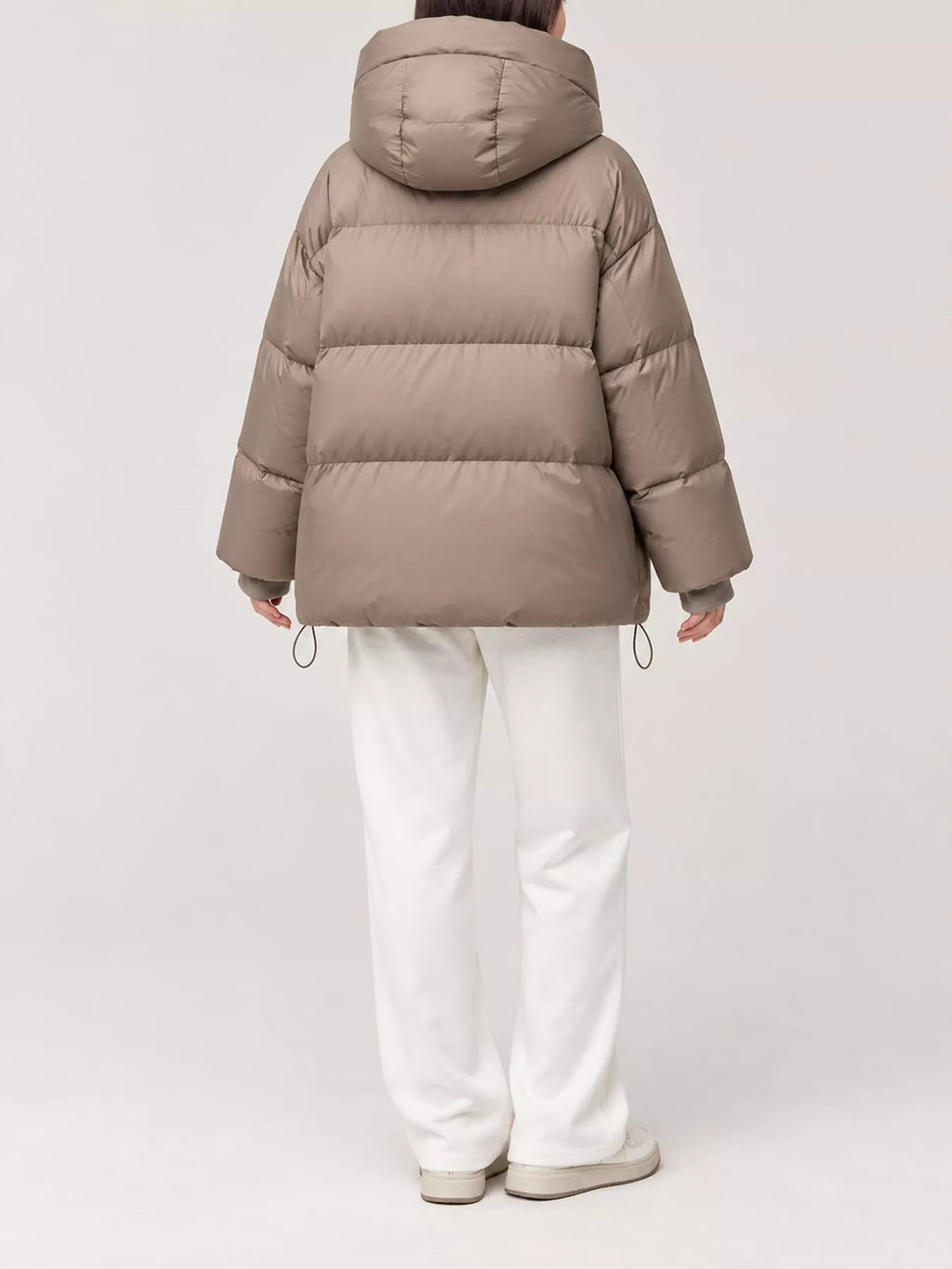 Back view of model in taupe quilted puffer jacket featuring horizontal baffles and adjustable hem drawstrings