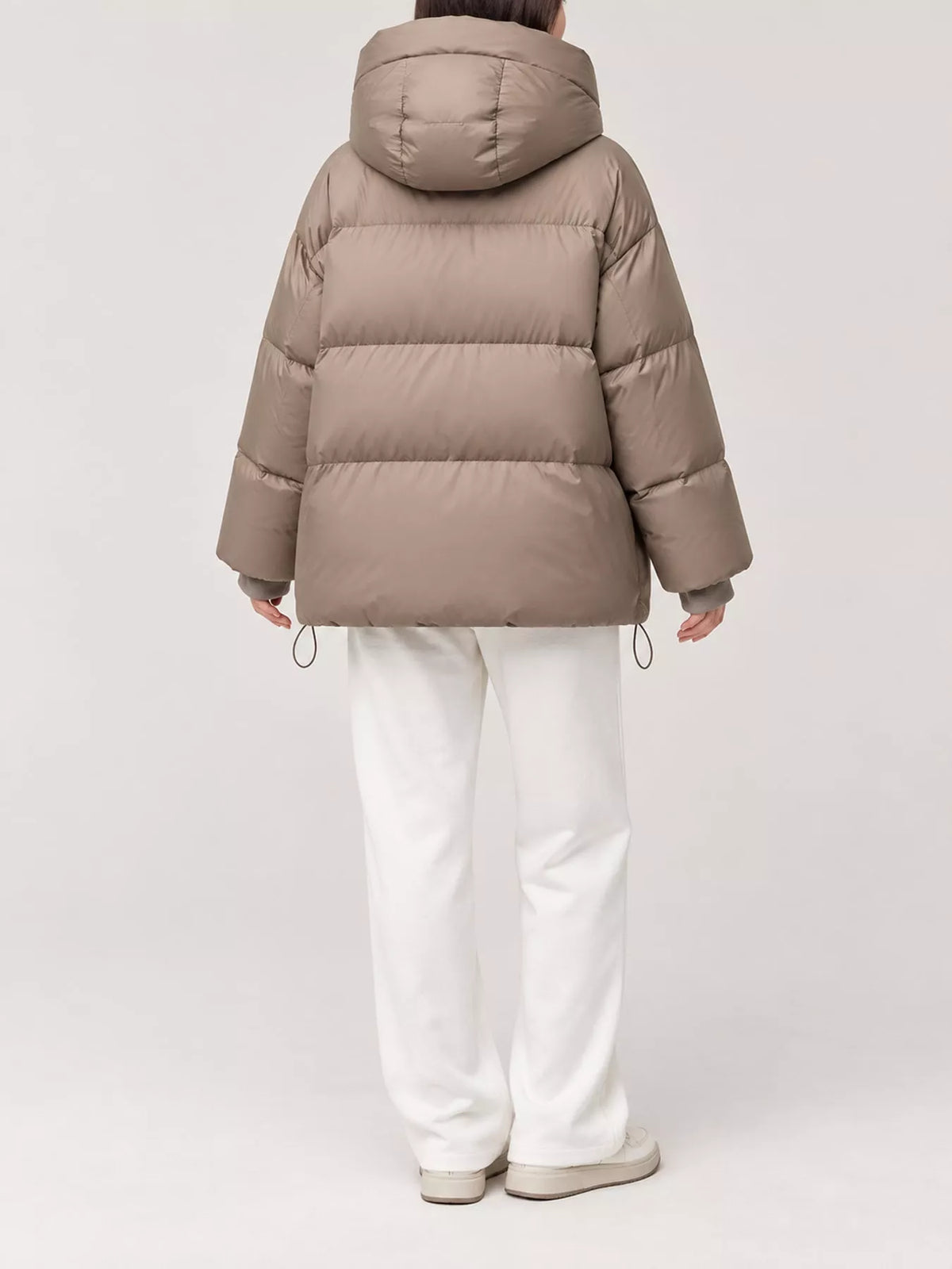 Back view of model in taupe quilted puffer jacket featuring horizontal baffles and adjustable hem drawstrings