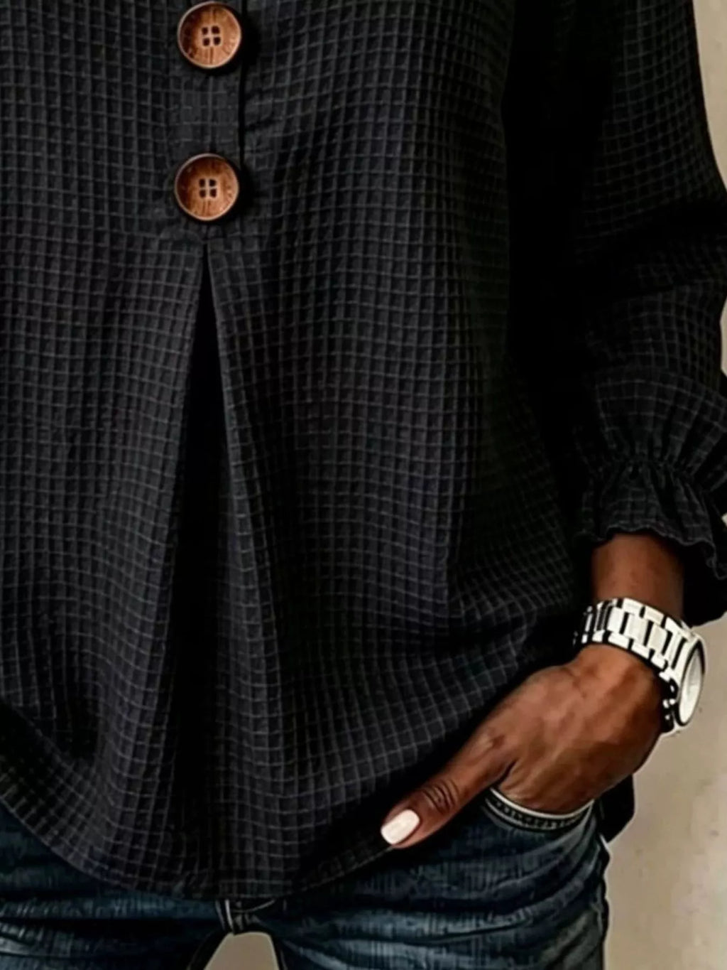 Detalle del puño fruncido de la manga de la blusa negra y mano en el bolsillo de los jeans