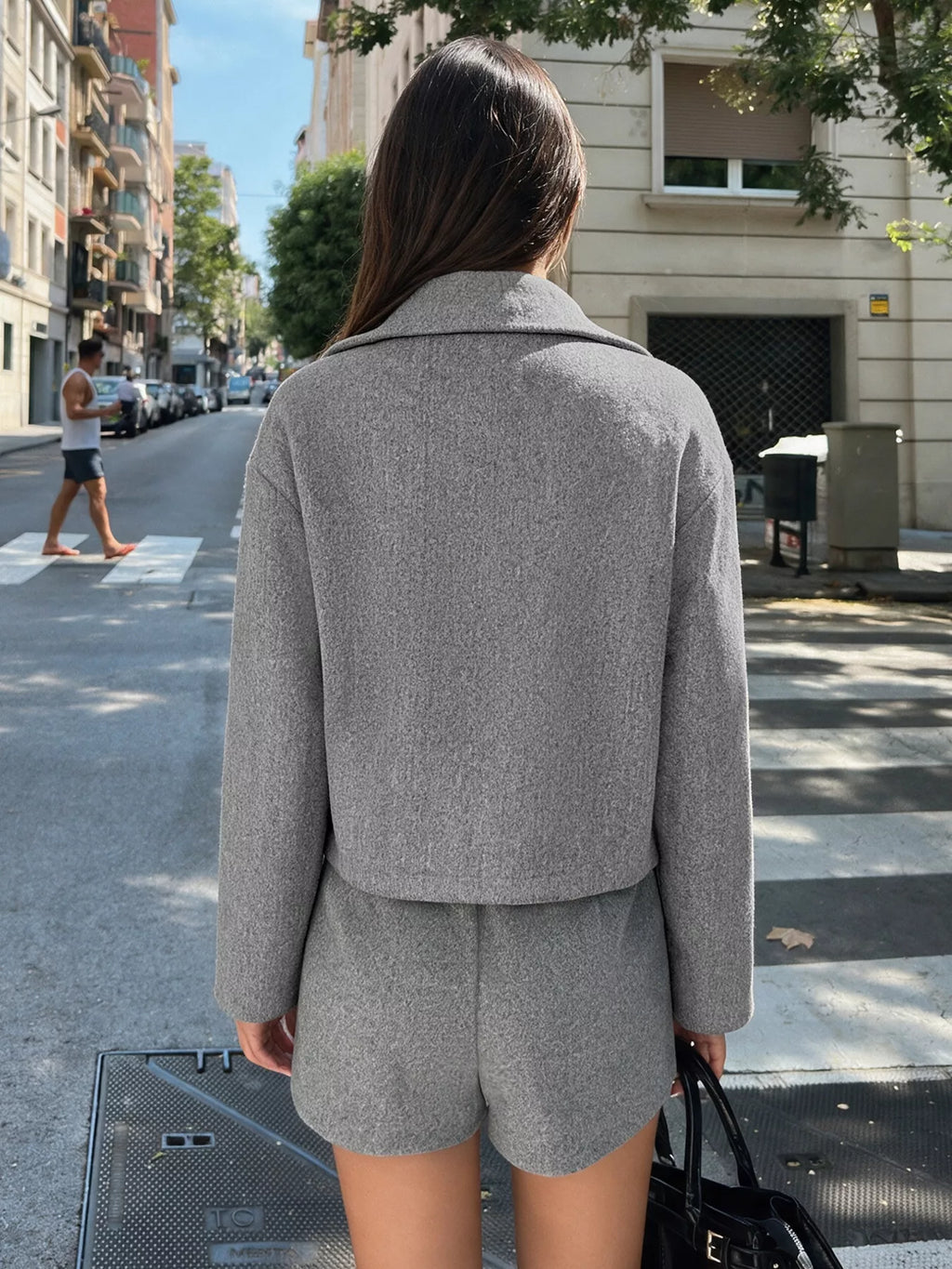 Rückansicht des Modells zeigt saubere Rückseite der grauen Perfee Cropped-Jacke und passende Shorts mit geradem Saum vor Stadthintergrund