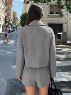 Rückansicht des Modells zeigt saubere Rückseite der grauen Perfee Cropped-Jacke und passende Shorts mit geradem Saum vor Stadthintergrund