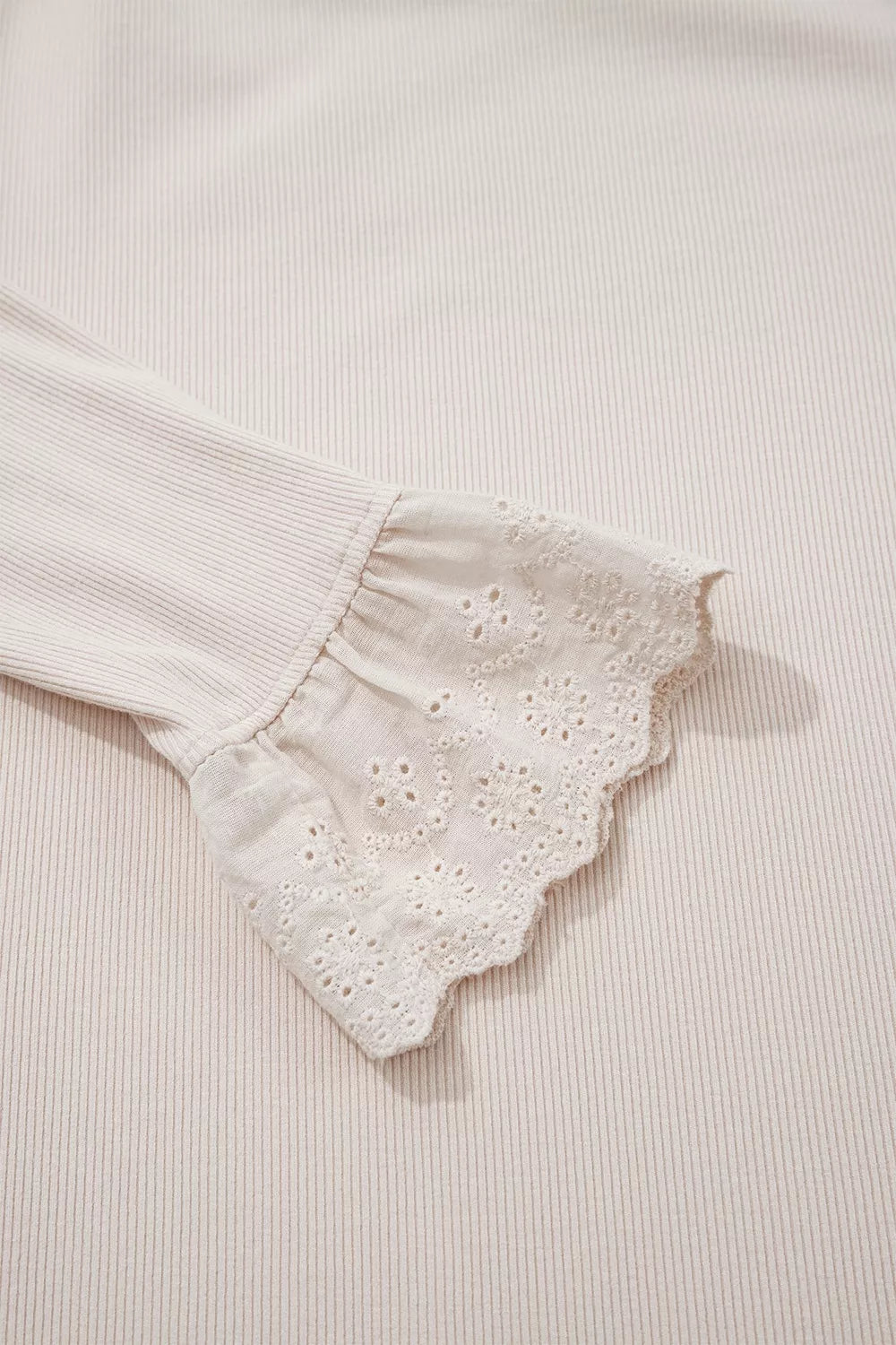 Macro shot of flared sheer eyelet lace ruffle cuff attached to ribbed sleeve