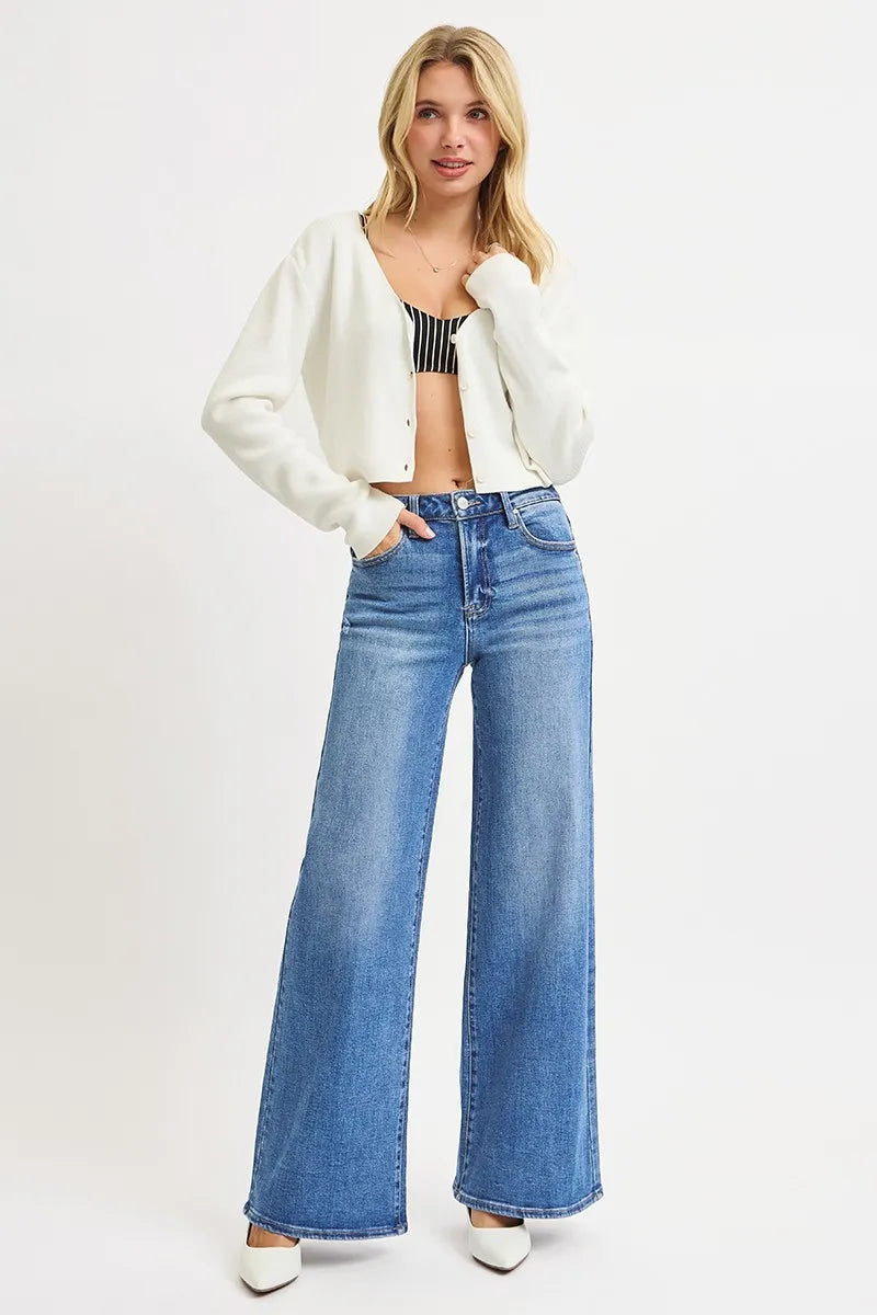 Model in medium blue high-rise wide-leg jeans styled with striped crop top, white cardigan, and pointed heels against white