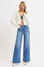 Model in medium blue high-rise wide-leg jeans styled with striped crop top, white cardigan, and pointed heels against white