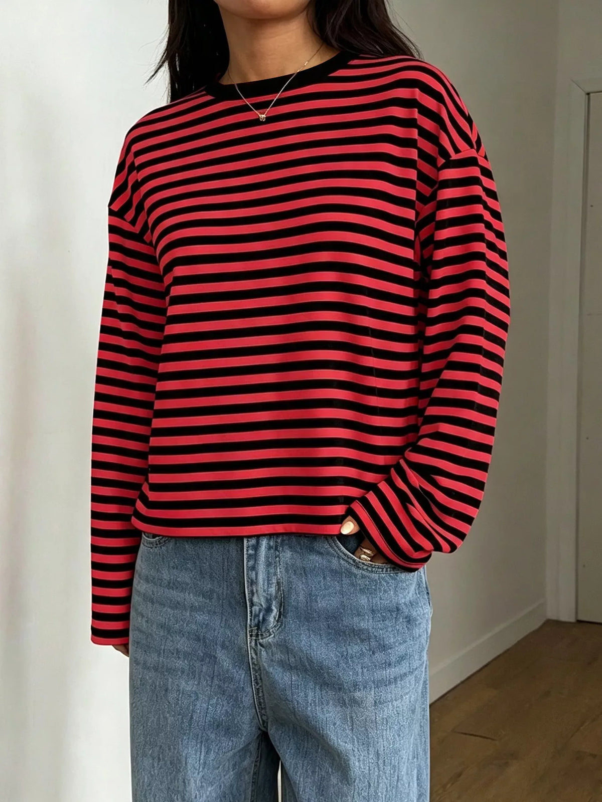 Modella in top maniche lunghe a righe rosse e nere con taschino dei jeans, silhouette casual