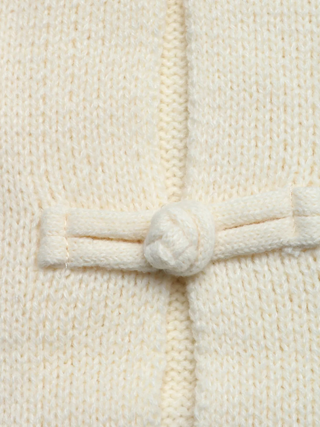 Extremnahaufnahme des filigranen, handgemachten Chinesischen Knotenknopfes an der Vorderseite der Strickjacke