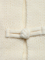 Extremnahaufnahme des filigranen, handgemachten Chinesischen Knotenknopfes an der Vorderseite der Strickjacke