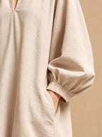 Gros plan de la mini-robe beige montrant le tissu froissé, le décolleté en V froncé et la main dans la poche latérale profonde