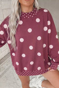Model in oversized maroon polka dot tunic sweatshirt with white sneakers against white brick wall