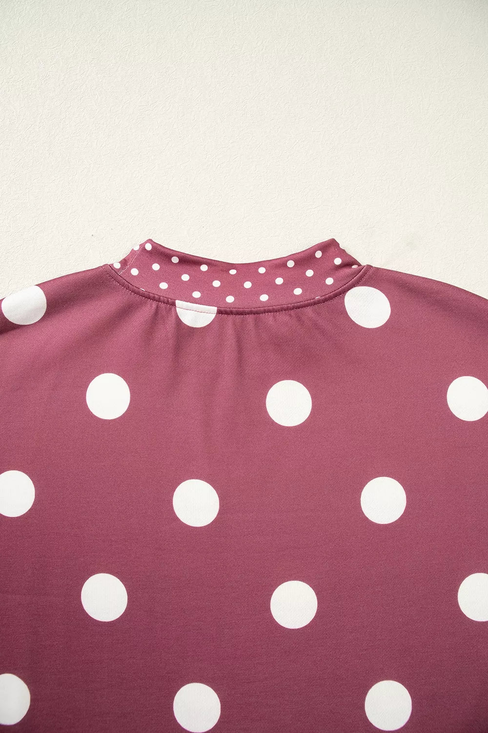 Detail shot of maroon knit texture and precise stitching of small dotted contrast trim at neckline