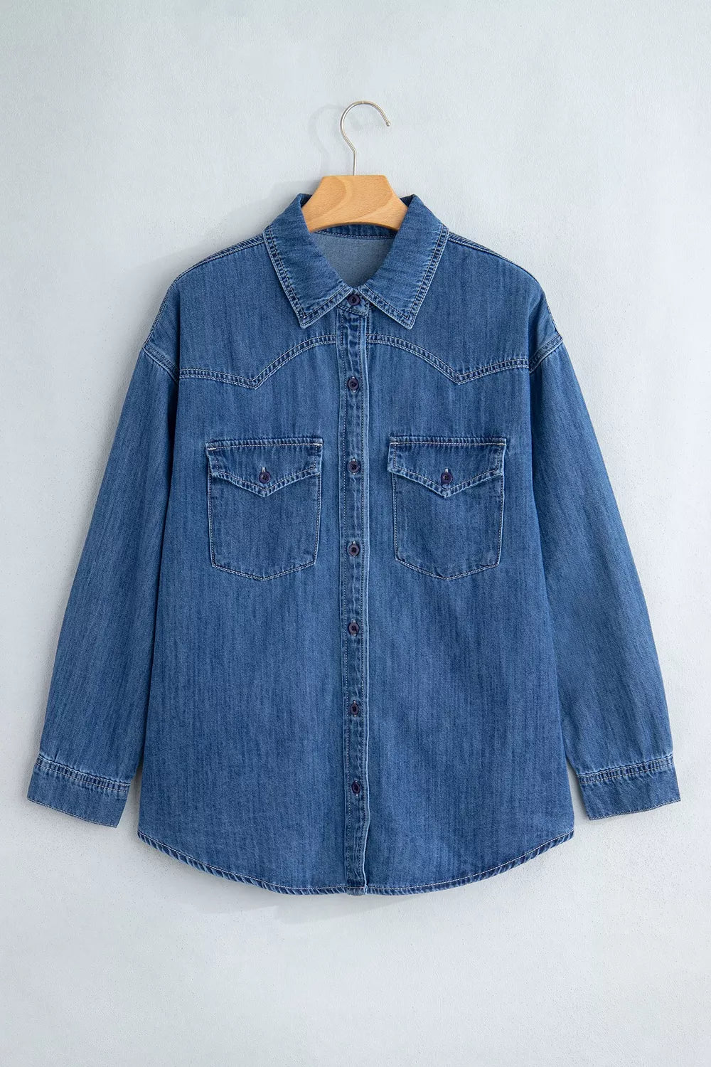 Camisa vaquera azul en percha: cuello puntiagudo, cierre completo, bolsillos parche y yoke vaquero distintivo.