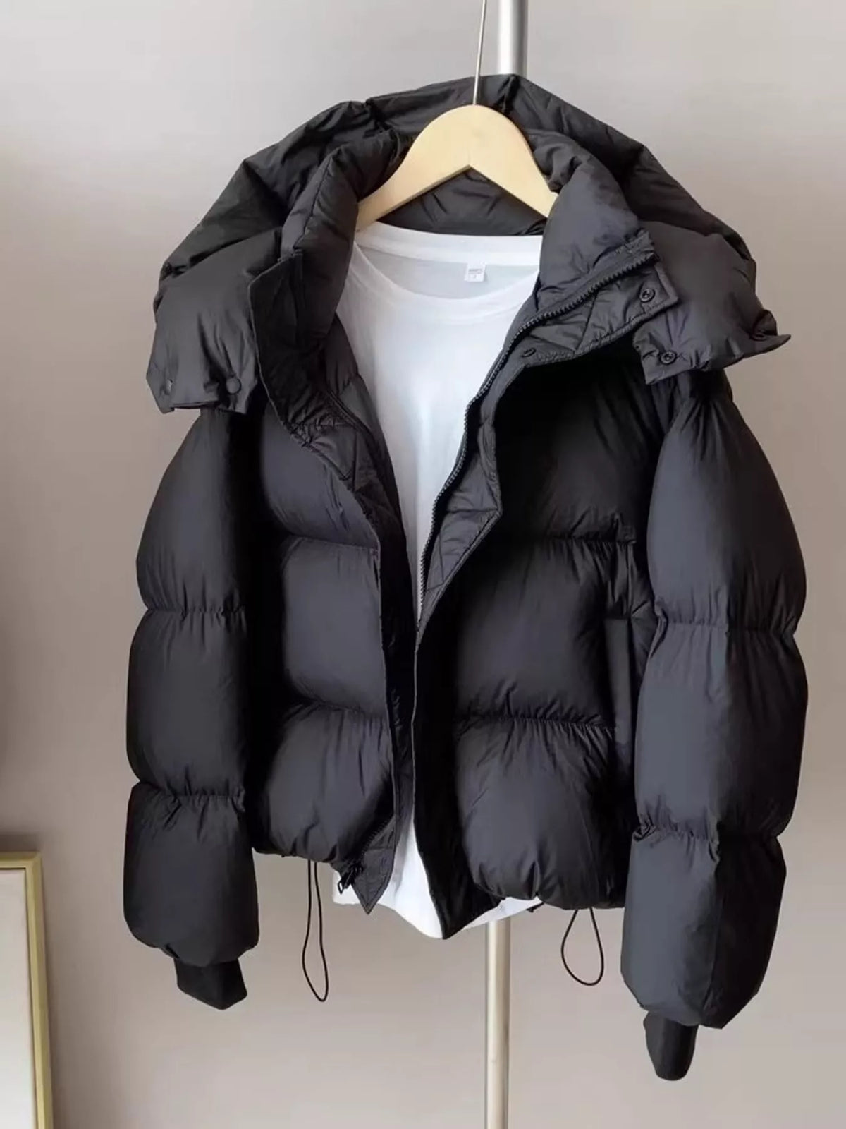 Black quilted hooded puffer jacket on wooden hanger showing horizontal baffle stitching and central zipper