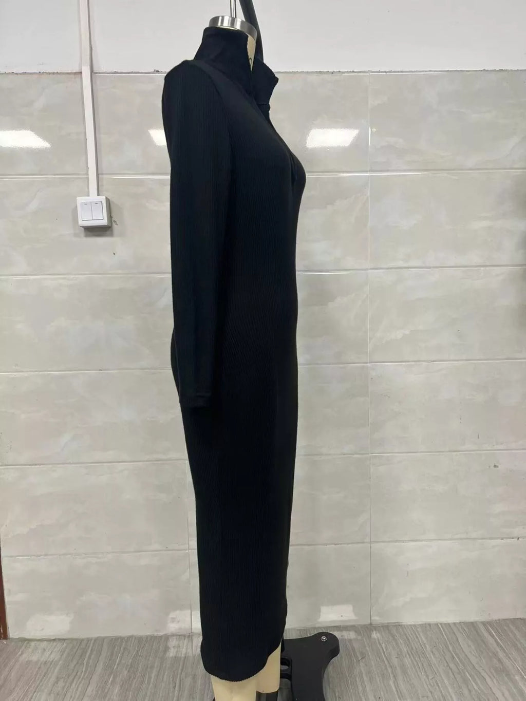 Profil latéral d'une robe pull tricotée côtelée noire sur mannequin soulignant l'élasticité, la profondeur du col V et l'ourlet midi droit
