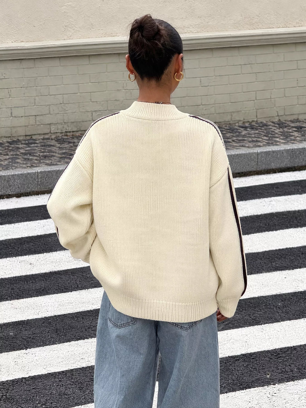Rückenansicht der oversized cremefarbenen Strickjacke mit dunkelbraunen Ärmelstreifen im Freien