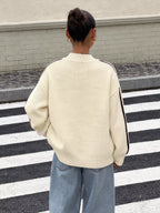 Rückenansicht der oversized cremefarbenen Strickjacke mit dunkelbraunen Ärmelstreifen im Freien