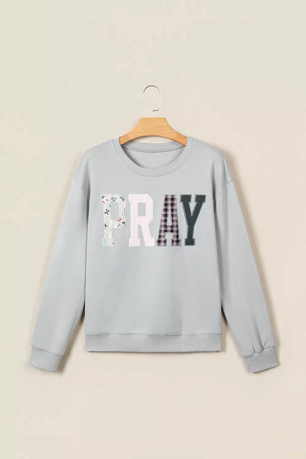 Flat-lay of light grey sweatshirt on wooden hanger. Displays distinct floral, striped, plaid, and solid textures of