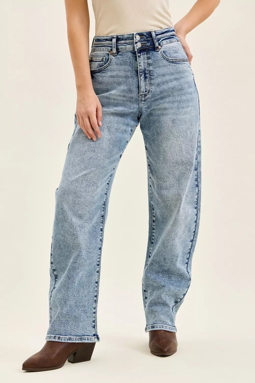 Light wash high-waist jeans with double-button waistband and arc-leg silhouette over brown cowboy boots