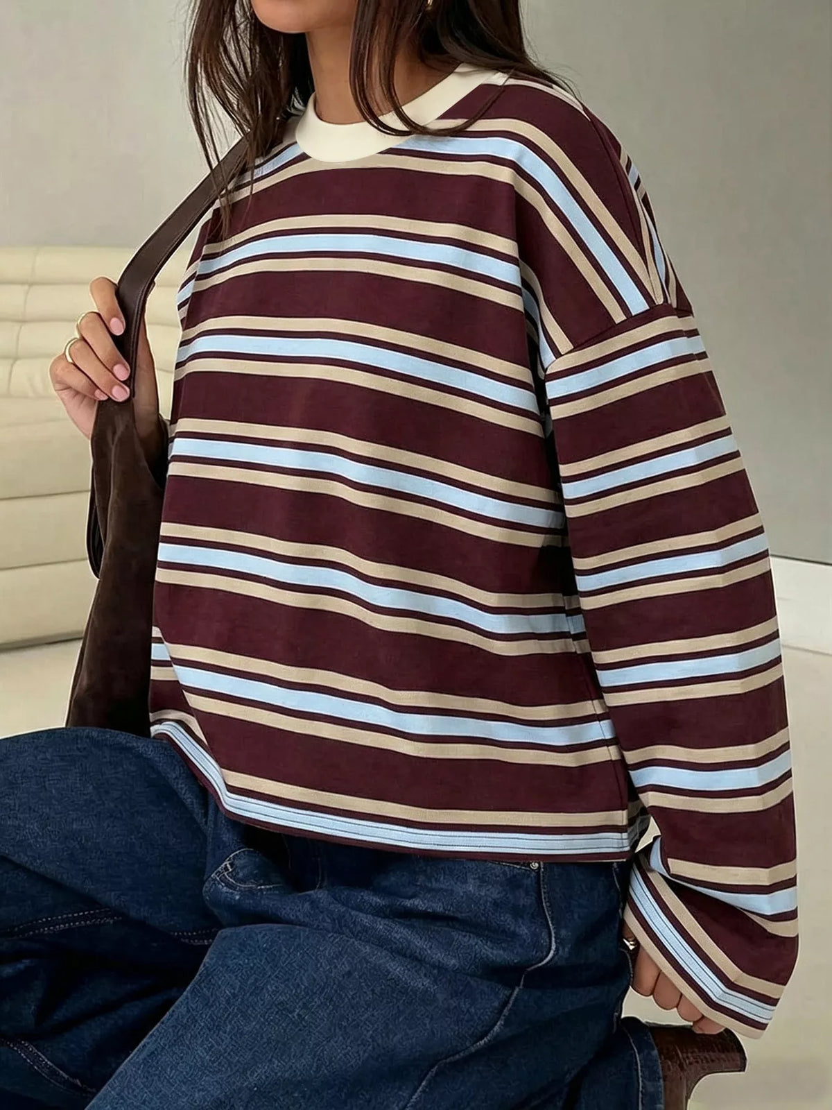 Modella seduta mostra top a righe base bordeaux con ampie bande azzurro e beige e collo tondo a coste crema contrastante