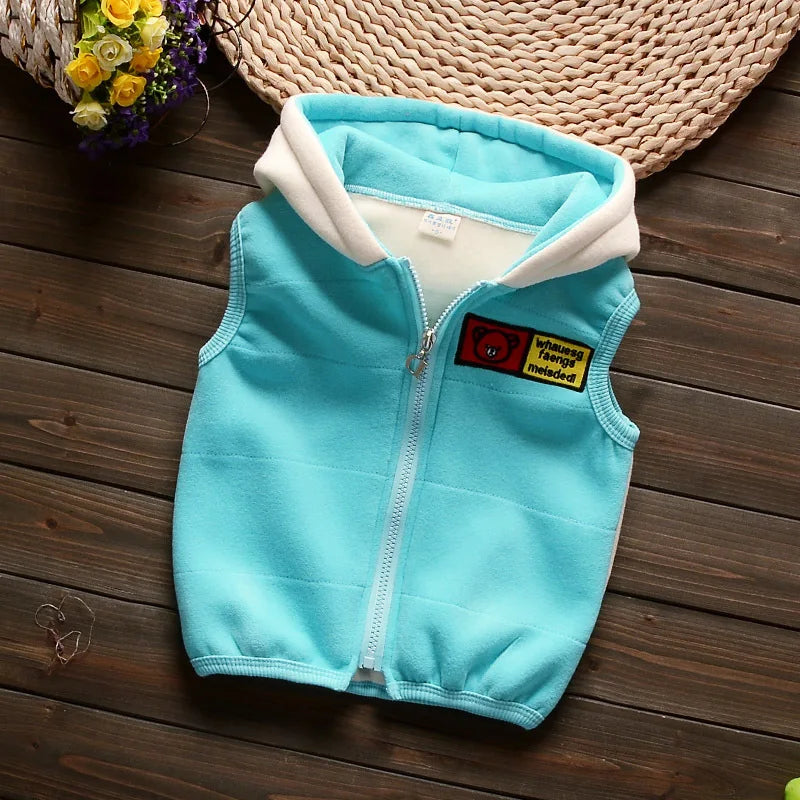 Top-down photo of light blue hooded vest on wood surface showing silver zipper, quilting lines, and patch