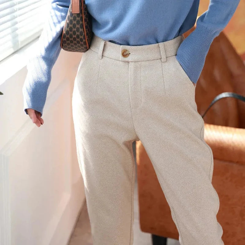 Look completo com calças lápis bege e suéter canalhado azul perto da janela