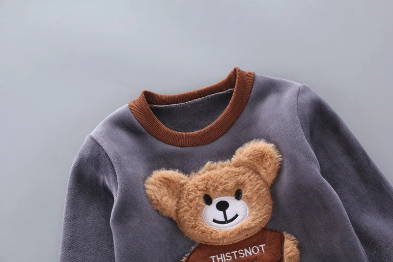 Close-up of grey sweatshirt showing soft fleece texture, ribbed collar, and detailed 3D plush bear applique