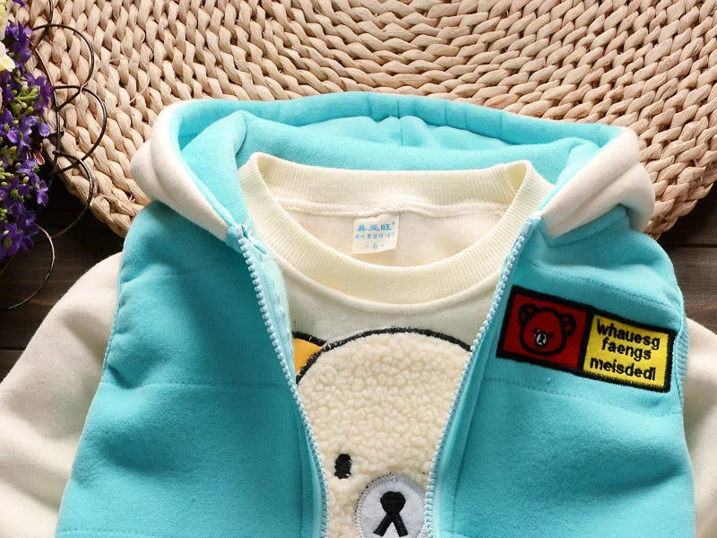 Close-up of blue vest over cream sweatshirt showing red bear icon patch, ribbed neckline, and basket background