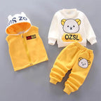 Flat lay of yellow and white children's outfit including bear-ear vest, graphic sweatshirt, and patched pants