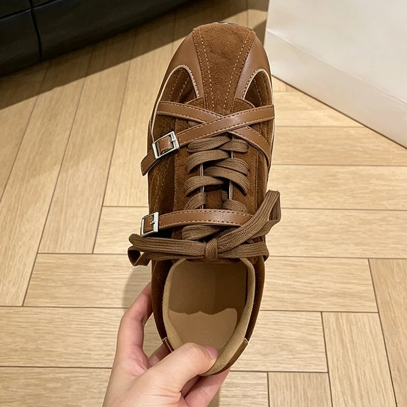 Top-down view of brown sneaker with mixed materials, cross-straps, and bow-tied laces on wood