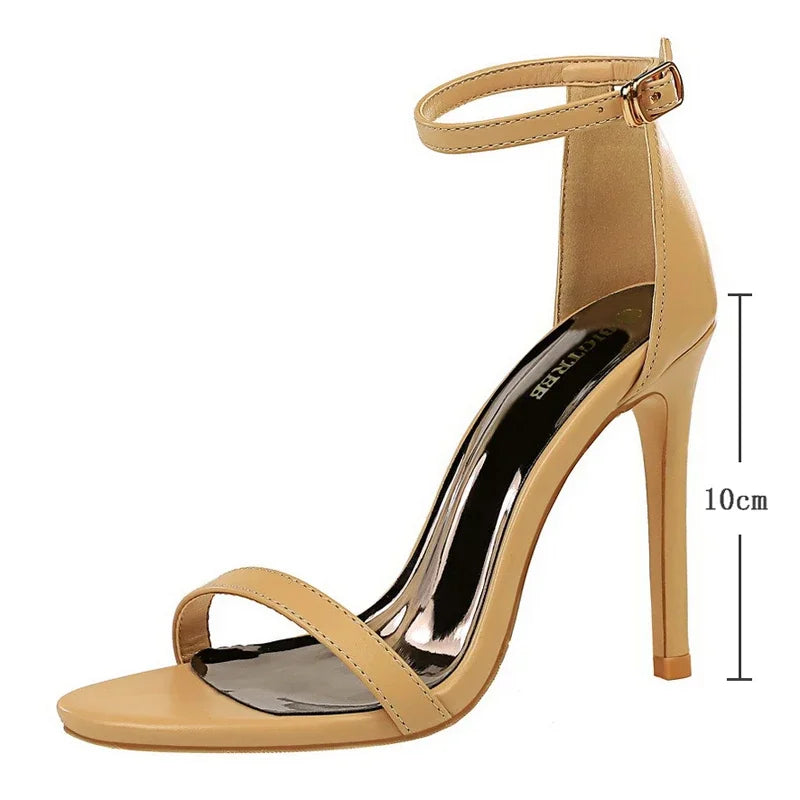 Vista lateral de sandália stiletto nude bege com bico quadrado aberto, tira fina e elegante alça de tornozelo dourada