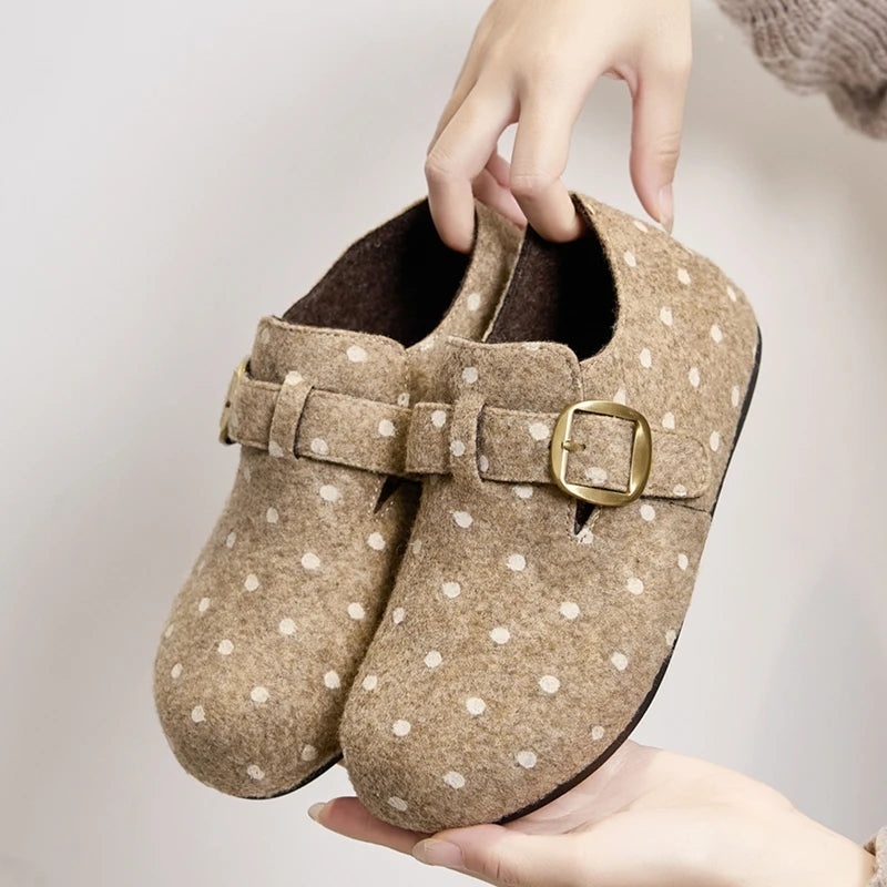 Manos sosteniendo clogs de fieltro beige para mostrar textura superior y hebilla metálica dorada