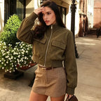 Jaqueta cropped estilo bomber em suede verde-oliva, gola alta, fecho de prata, bolsos com aba e punhos canelados.