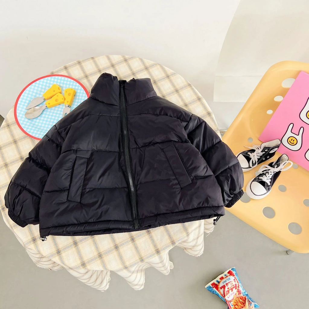 Black quilted jacket on plaid table with props like cheese cutlery and mini sneakers highlighting elastic cuffs.