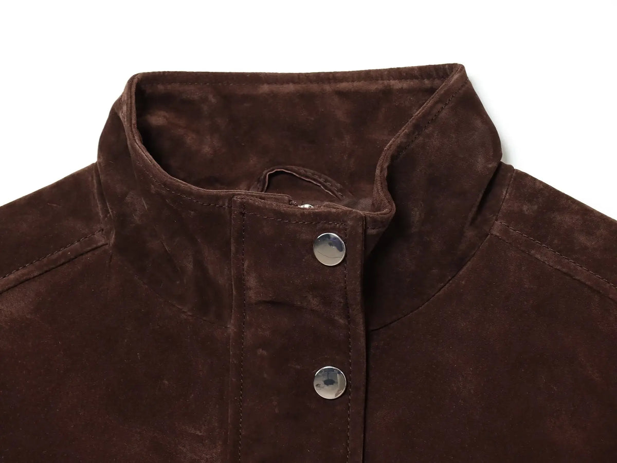 Detalhe da gola alta levantada da jaqueta castanha-escura com textura suave estilo suede e botões de pressão prateados.
