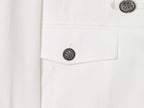 Detalhe do bolso no peito com aba pontiaguda presa por botão prateado gravado, destacando a textura do tecido branco tecido