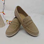 Mocassini cow suede incrociati color cammello che mostrano finitura opaca e ricamo patchwork accanto a un accessorio floreale