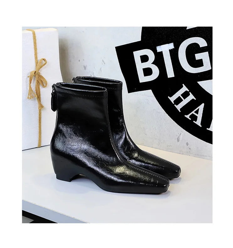 Botas pretas estilo retro enrugadas com bico quadrado e zíper lateral sobre superfície branca