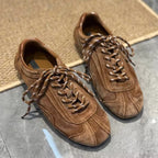 Brown flat sneakers on stone floor next to rug highlighting round toe shape