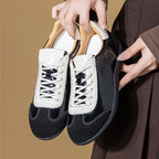Primer plano de zapatillas negras sujetadas por manos mostrando parte superior brillante, puntera de ante y panel de cordón cosido en zigzag