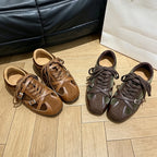 Two pairs of brown and olive green flat shoes with round toes and decorative buckle straps
