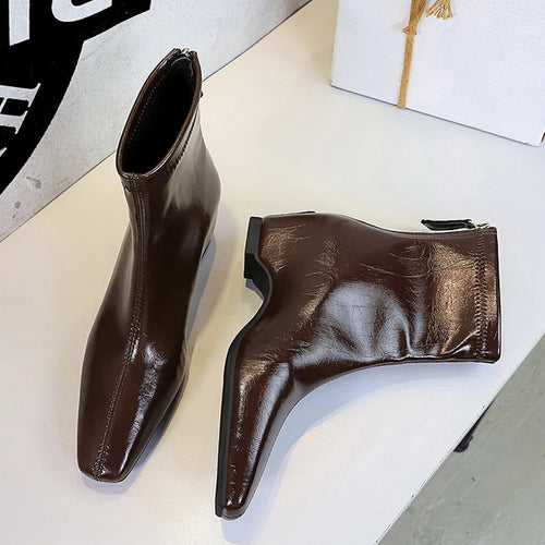 Botas curtas marrons brilhantes em PU com bico quadrado e zíper lateral sobre fundo branco