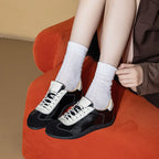 Zapatillas patchwork negras y crema usadas con calcetines acanalados descansando sobre silla de terciopelo naranja